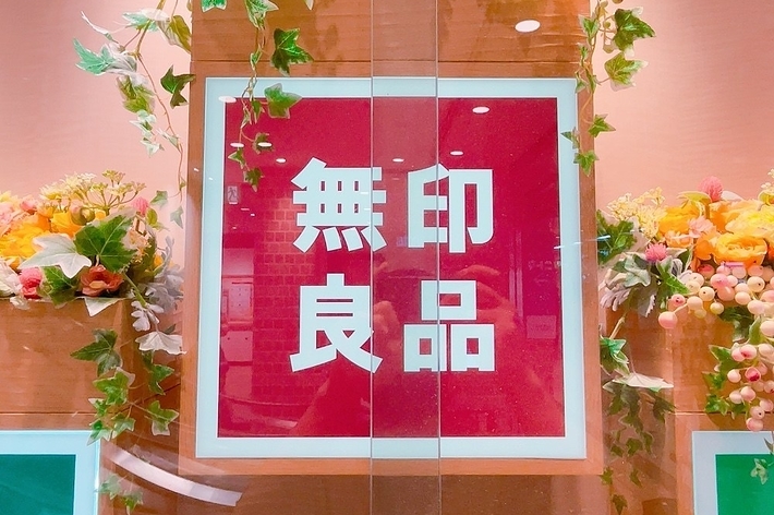 無印良品のロゴが飾られた店内ディスプレイ。周りには装飾用の花と葉が配置されている。