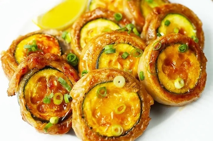 白い皿に盛られたレモンのくし切りと一緒に、ネギのトッピングされた焼きなすの料理。