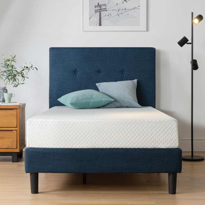 A neatly made bed with a blue headboard and simple frame in a well-lit room with decor