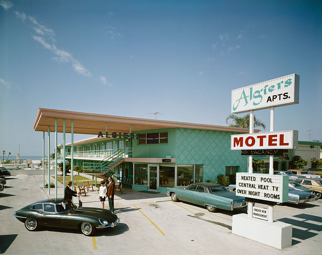 Vintage photo of people by classic cars in front of Algiers Motel with retro signage