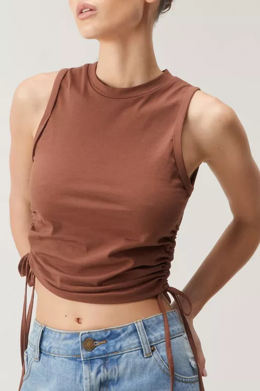 Person wearing a brown sleeveless cropped top with side ties, paired with denim. The focus is on the outfit&#x27;s details