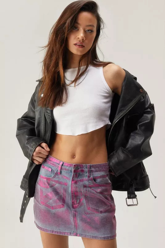 Woman in a crop top and pink printed skirt with an oversized jacket, posing for a shopping article
