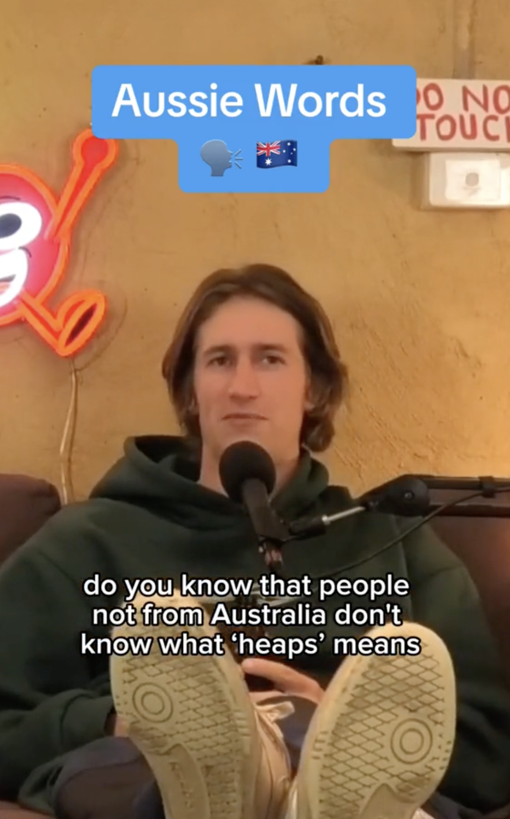 Person wearing a hoodie sits on a couch, text overlay discussing the Australian word &quot;heaps.&quot;