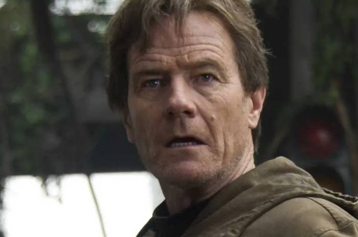 Bryan Cranston with a concerned expression in a brown jacket, outdoors