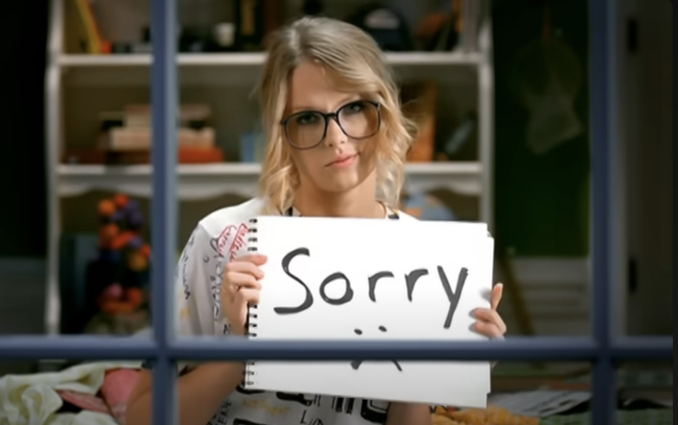 Woman holding a sign that reads "Sorry" in front of a window
