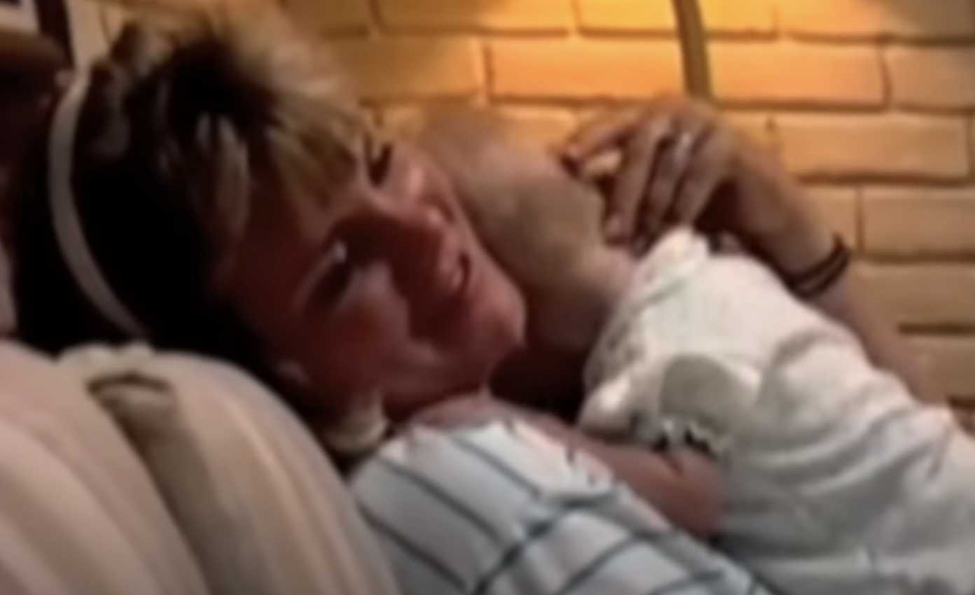 Woman lying down holding a baby, both appearing content, in a warm indoor setting