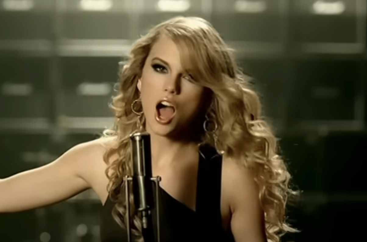 Person singing into microphone, wearing sleeveless top and hoop earrings