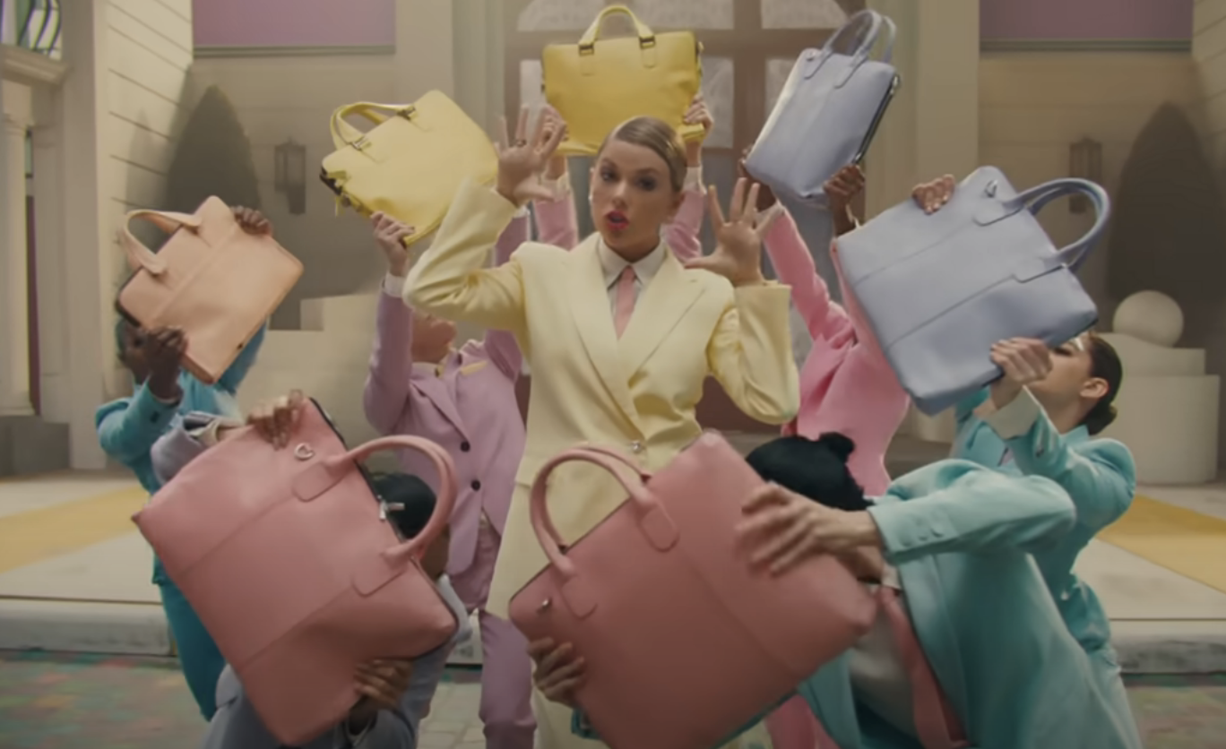 Woman in yellow suit surrounded by people holding pastel handbags in a choreographed pose