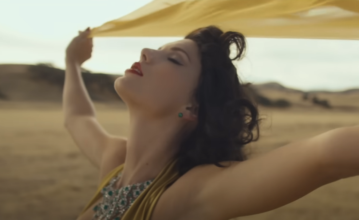 Woman in a patterned dress holding a yellow fabric above her head in a field