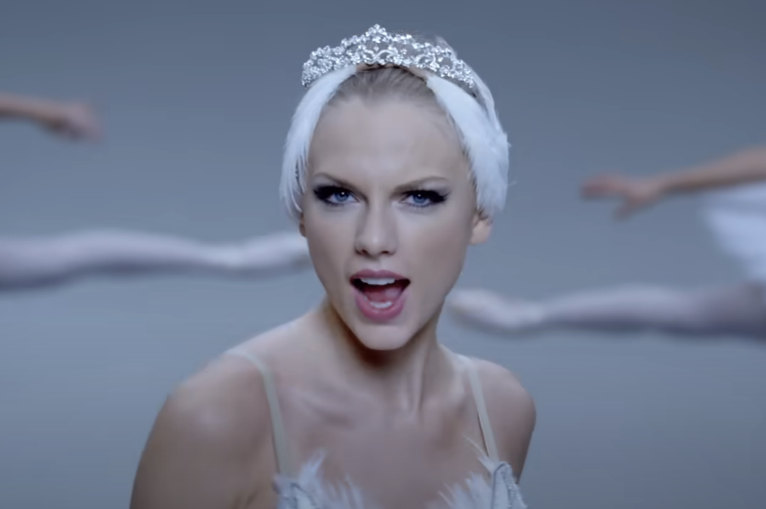 Taylor Swift in a music video, wearing a tiara and an off-the-shoulder top