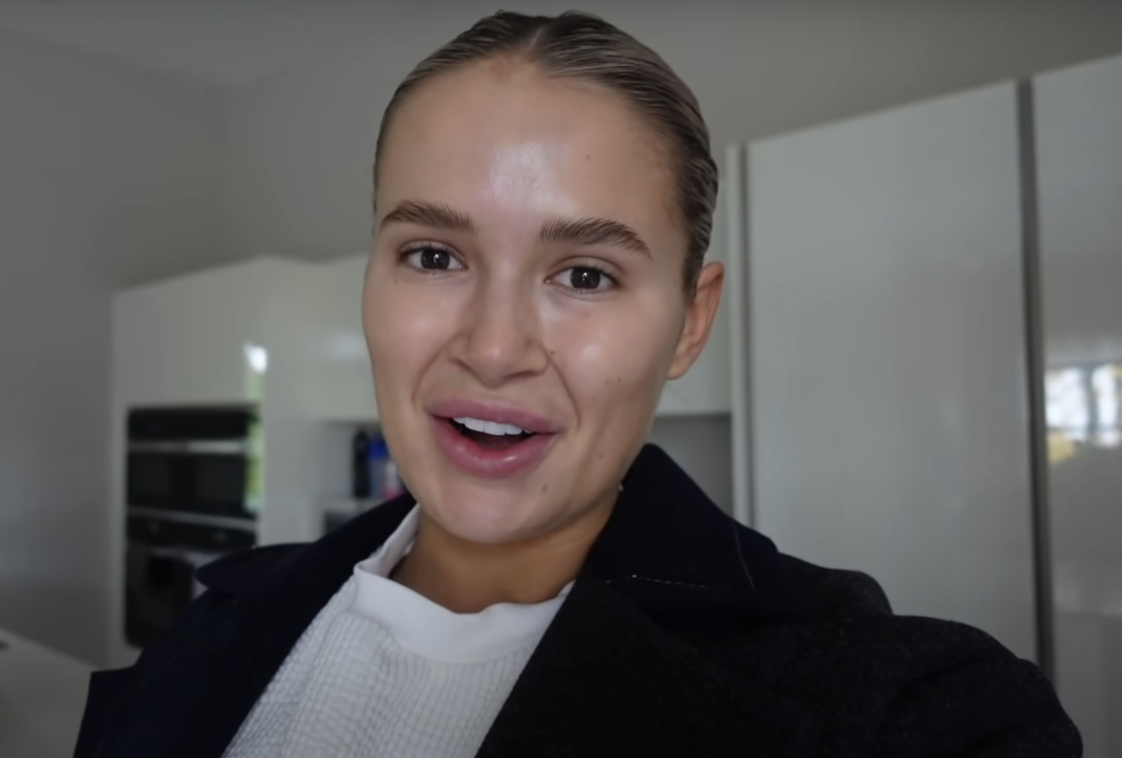 Close-up of a smiling Molly-Mae with her hair pulled back, wearing a top and dark coat