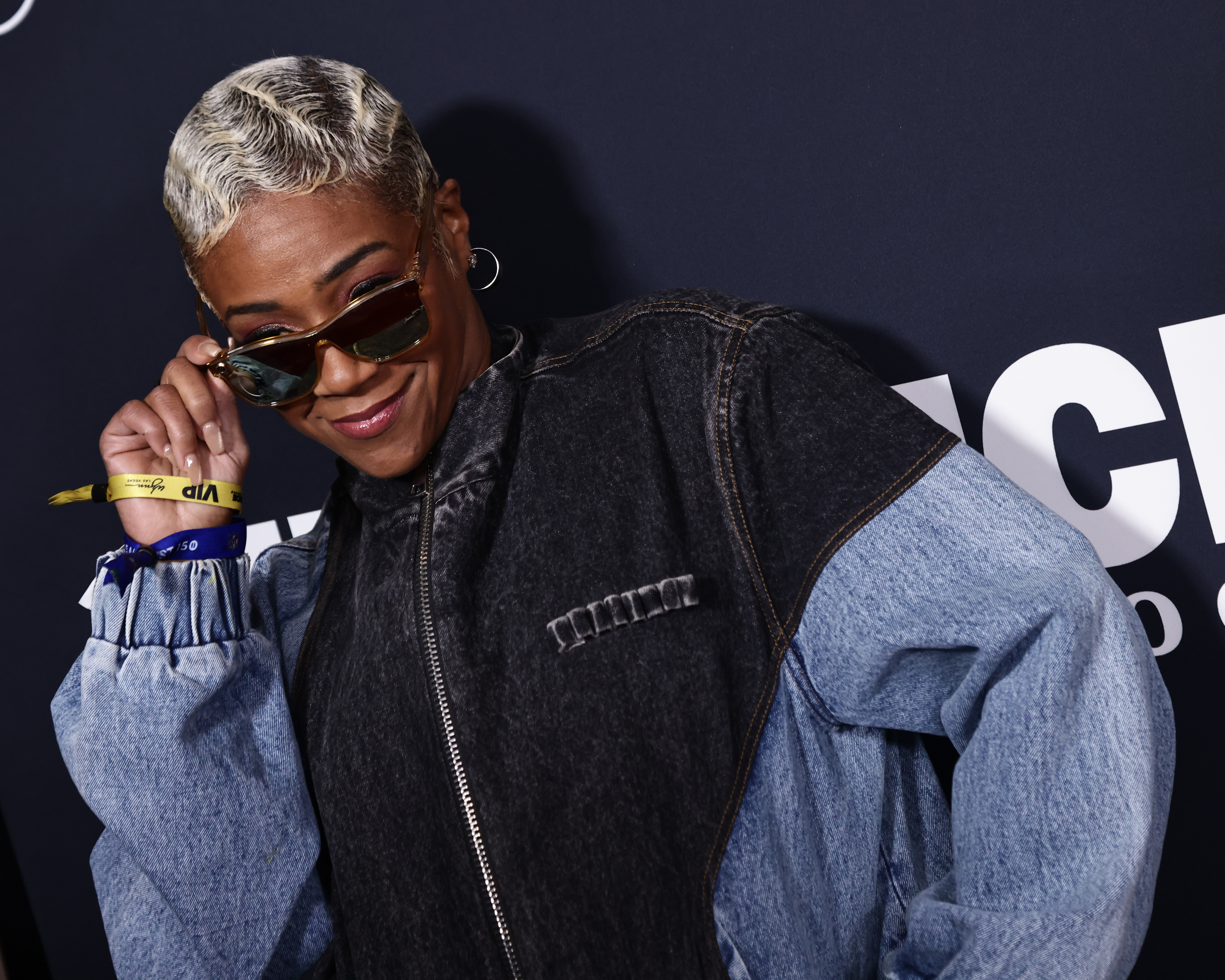 Tiffany Haddish posing confidently, wearing a denim jacket, with sunglasses and hoop earrings