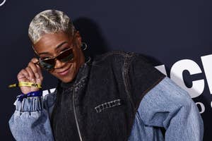 Tiffany Haddish posing confidently, wearing a denim jacket, with sunglasses and hoop earrings