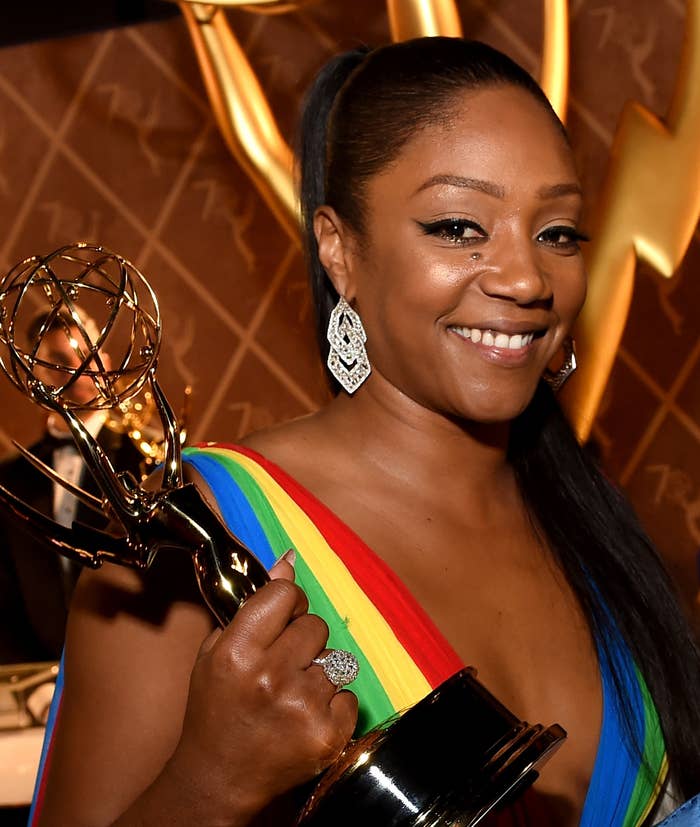 Tiffany Haddish in a striped dress holding an Emmy award, smiling