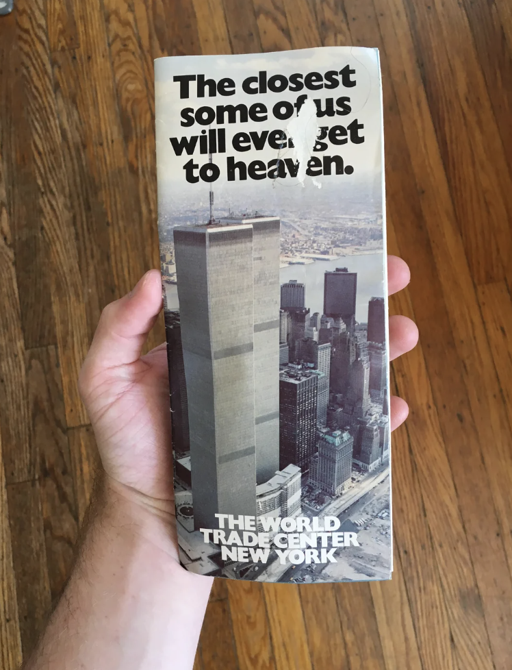 Hand holding a brochure with an image of the Twin Towers captioned, &quot;The closest some of us will ever get to heaven. THE WORLD TRADE CENTER NEW YORK&quot;