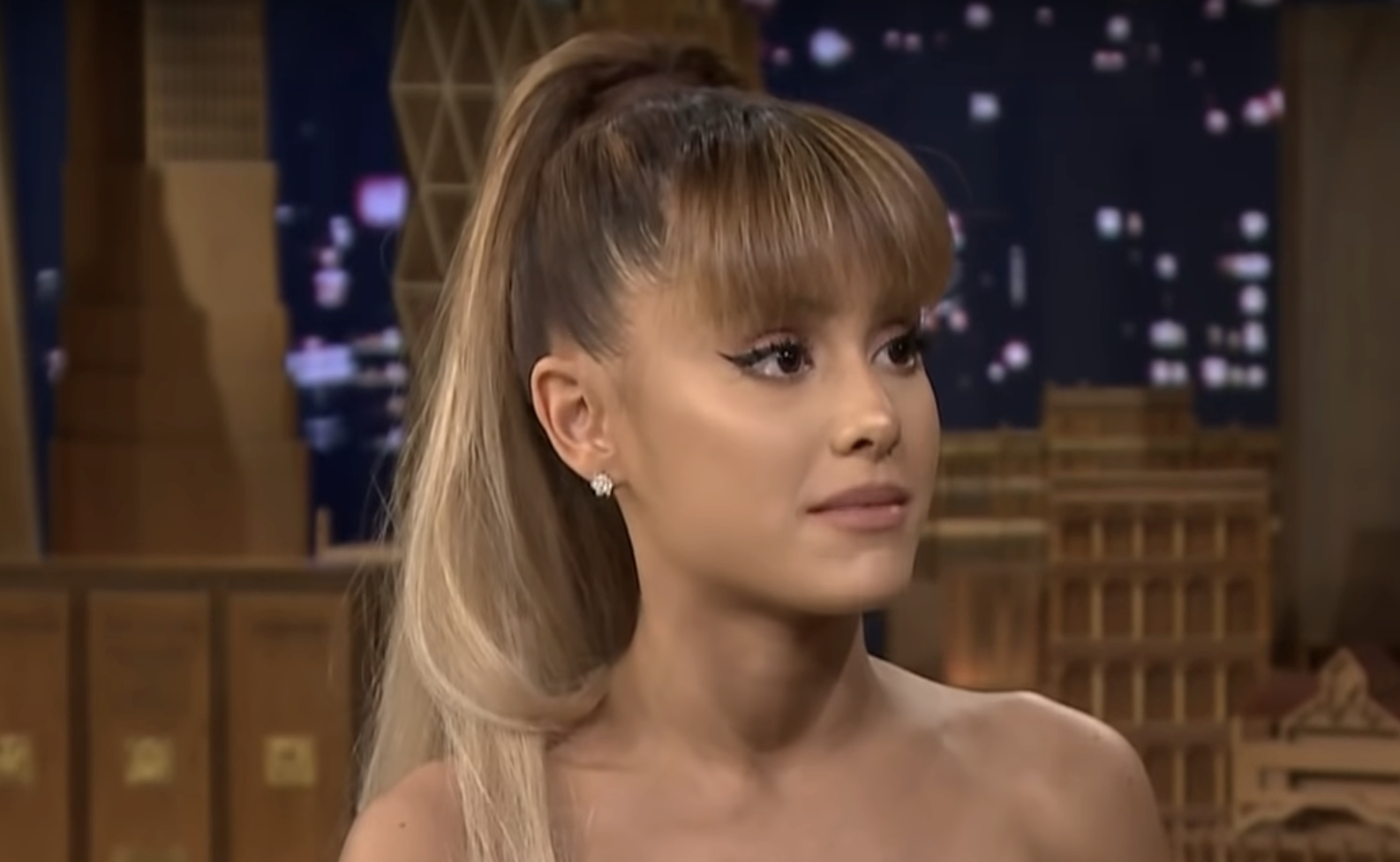 Close-up of Ariana Grande with a high ponytail and strapless outfit, looking to the side