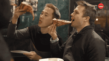 Two people enjoying a slice of pizza, one folding it before taking a bite