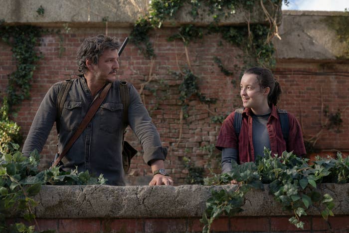 Pedro Pascal and Bella Ramsey in &quot;The Last of Us&quot; as Joel and Ellie, standing by a wall with foliage
