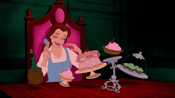 Animated character Belle holding a plate with a cupcake, with more treats on a table