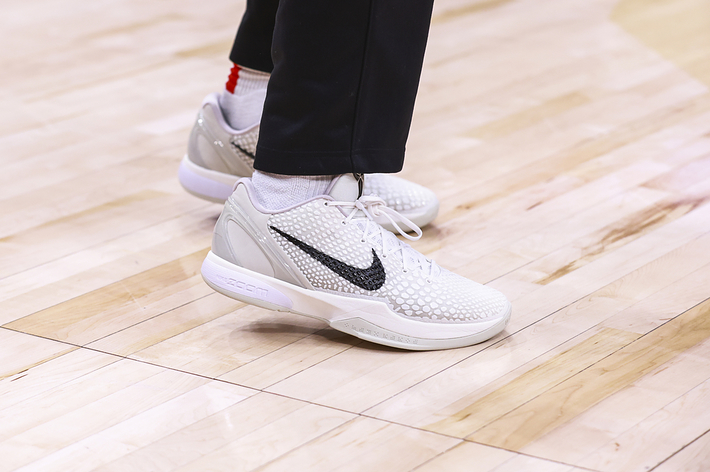 Close-up of a person's feet wearing white-patterned sneakers and black pants on a basketball court