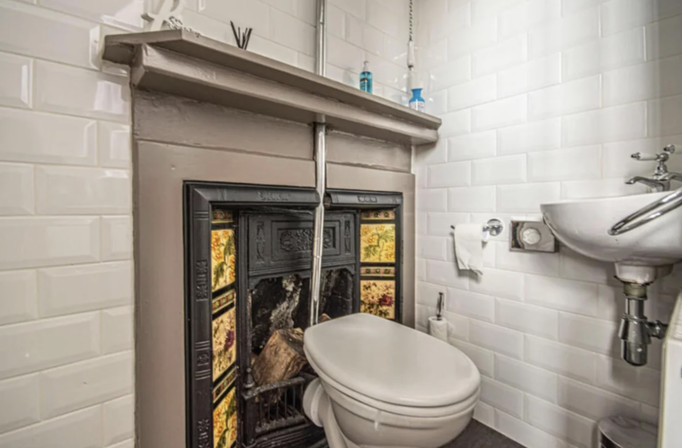 A bathroom with a decorative fireplace behind a toilet and wall-mounted sink