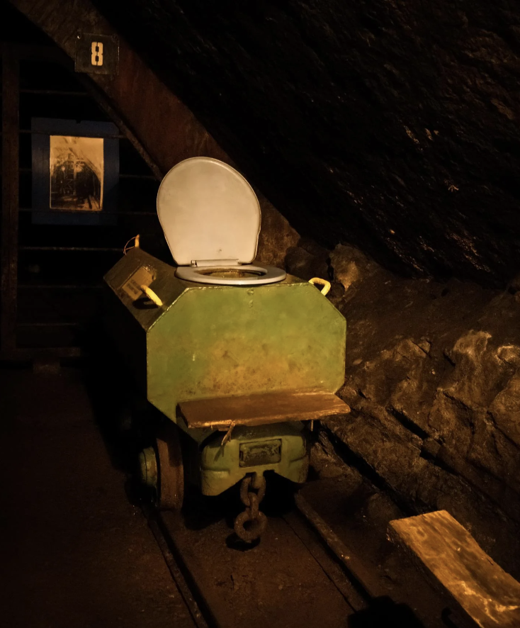 Antique wooden toilet cart with a hinged lid, set in a dimly lit, rustic underground space