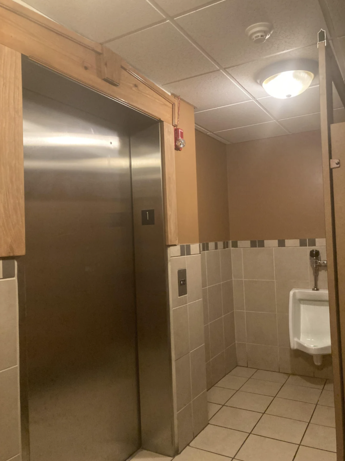 Elevator that opens inside of a bathroom next to a urinal