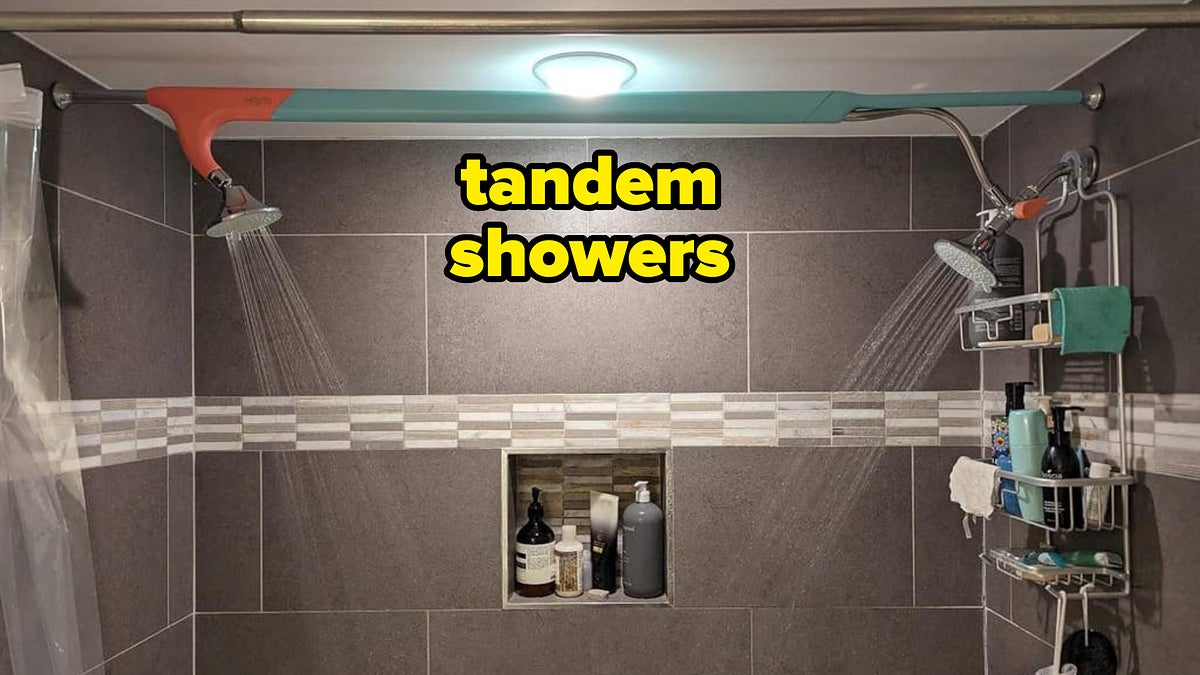 Two showerheads on opposite walls in a tiled shower with shelves of bath products
