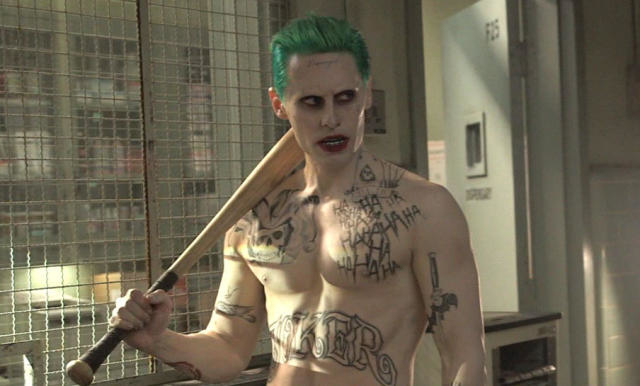 Joker character from movie, holding a bat, with tattoos, shirtless, in front of a fence