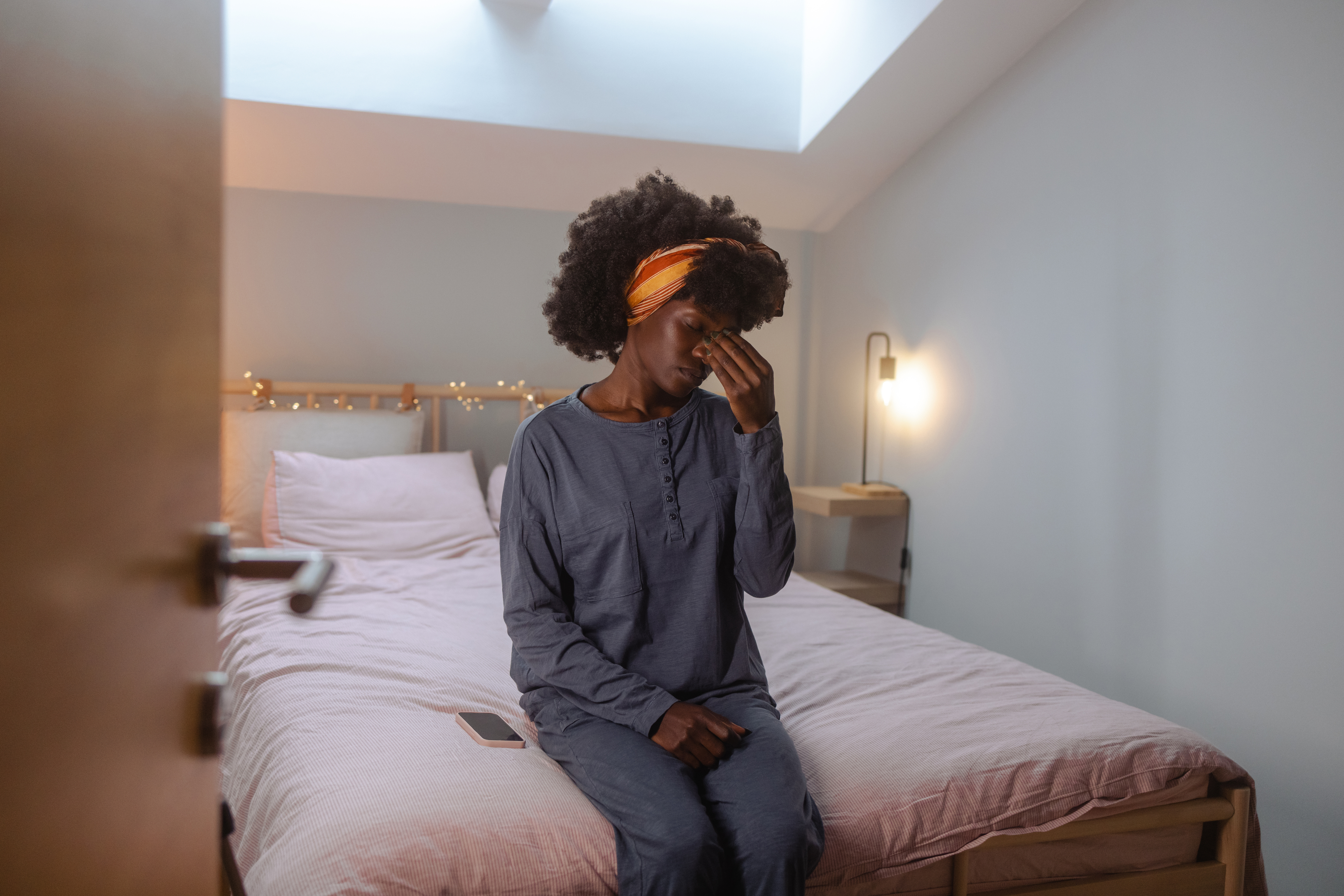 Person sitting on bed with hand on forehead in a gesture of stress or headache