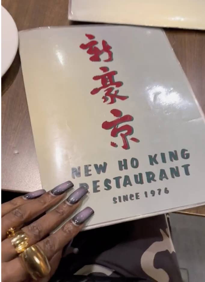 Hand holding a restaurant menu titled &quot;New Ho King Restaurant Since 1976&quot; with Chinese characters above English text