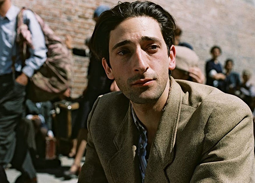 Man in a casual jacket seated outdoors, blurred background, looking thoughtful