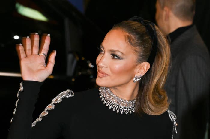 Jennifer Lopez wearing a black long-sleeve dress with jeweled neckline, waving hello