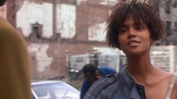 Halle Berry in character with a short, spiky hairstyle, wearing a strap dress on a movie set