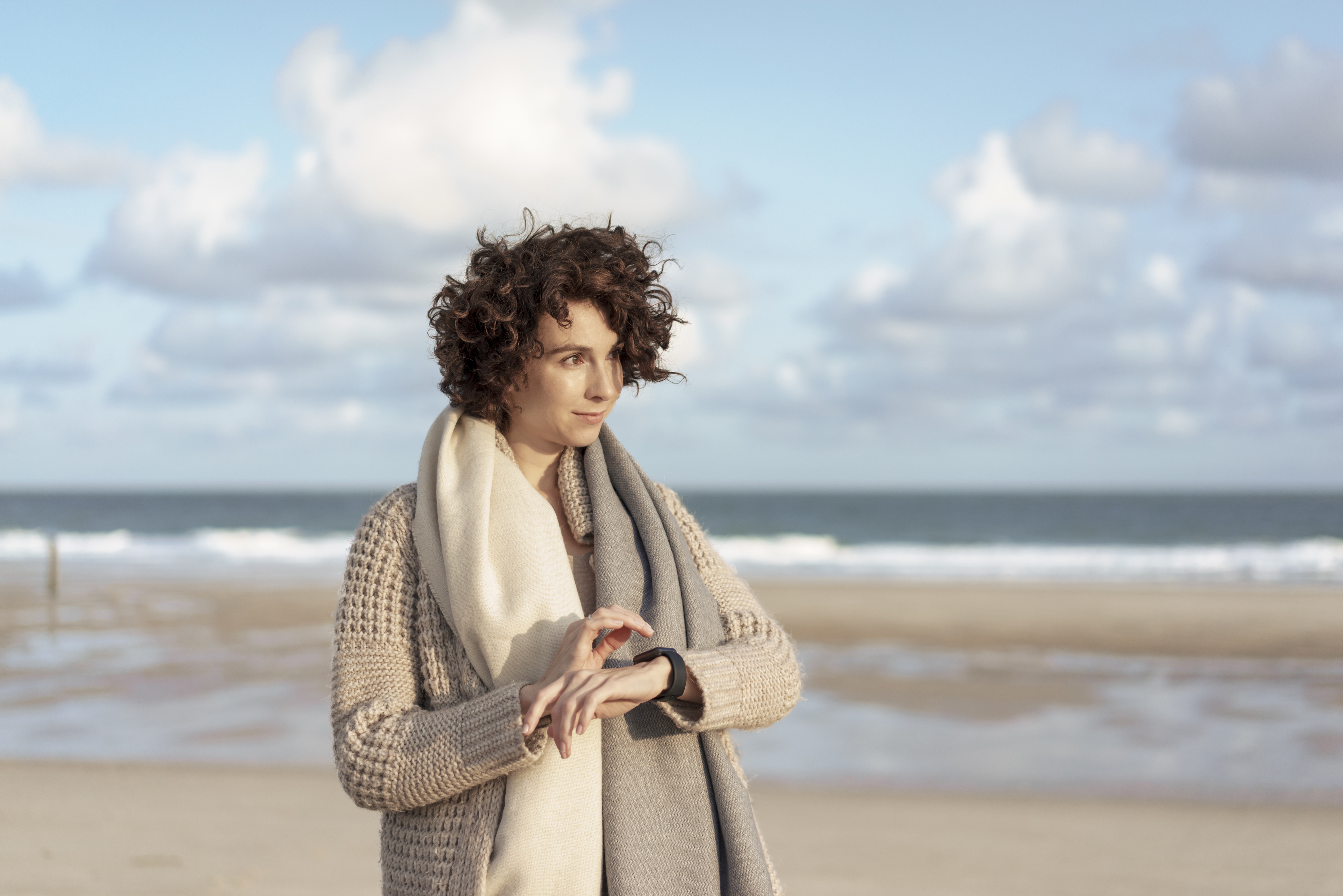 Person standing on the beach wearing a sweater and a scarf, with a contemplative look