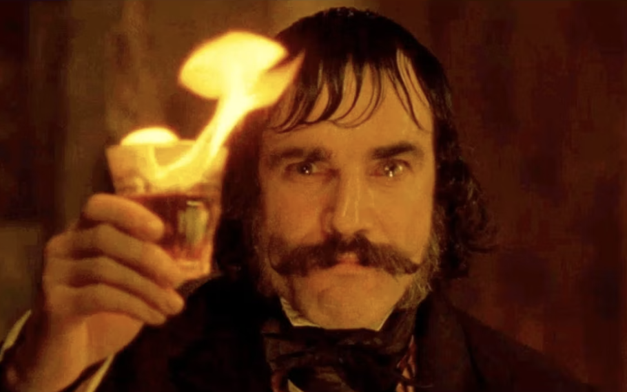 Character in period attire raising a flaming drink, with intent expression