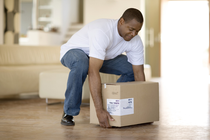 Person lifting a box using proper technique by bending their knees in a home setting