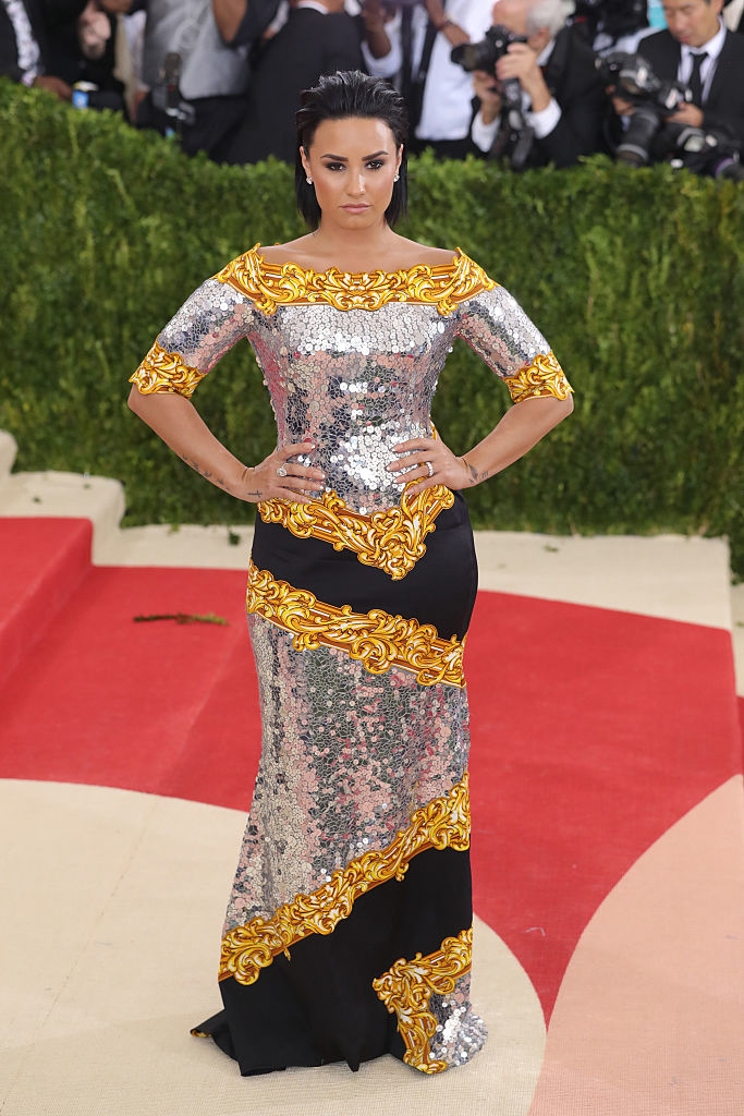 Demi Lovato poses on the red carpet in a fitted, sequined gown with embellishments