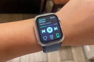 Person wearing Apple watch displaying Spotify music controls on screen