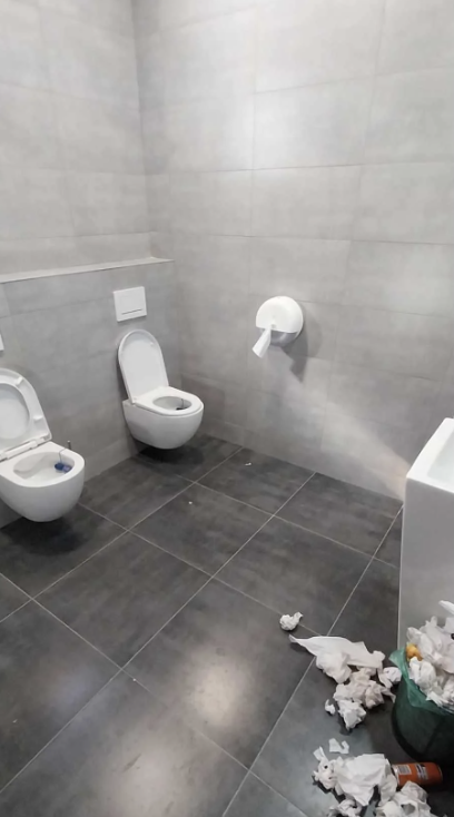 Bathroom with two toilets positioned so that only one can reach the toilet paper