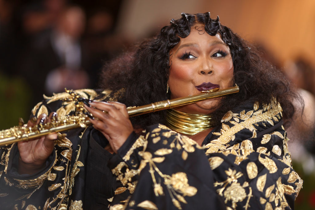 Lizzo in an embellished outfit playing a golden flute at a gala event