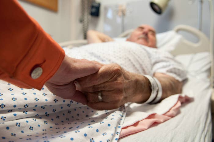 Person holding an elderly patient&#x27;s hand in a hospital bed, conveying care and support
