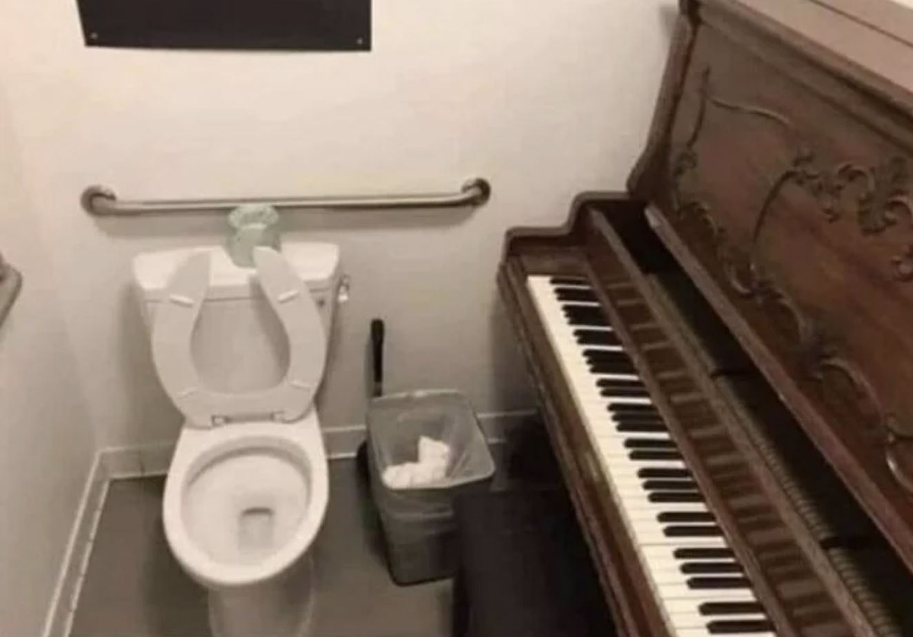 Bathroom with a toilet next to an upright piano, suggesting a quirky and humorous combination in a small space