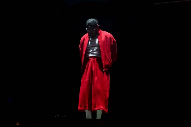 Music artist on stage wearing a shiny top and red robe, immersed in a dramatic spotlight