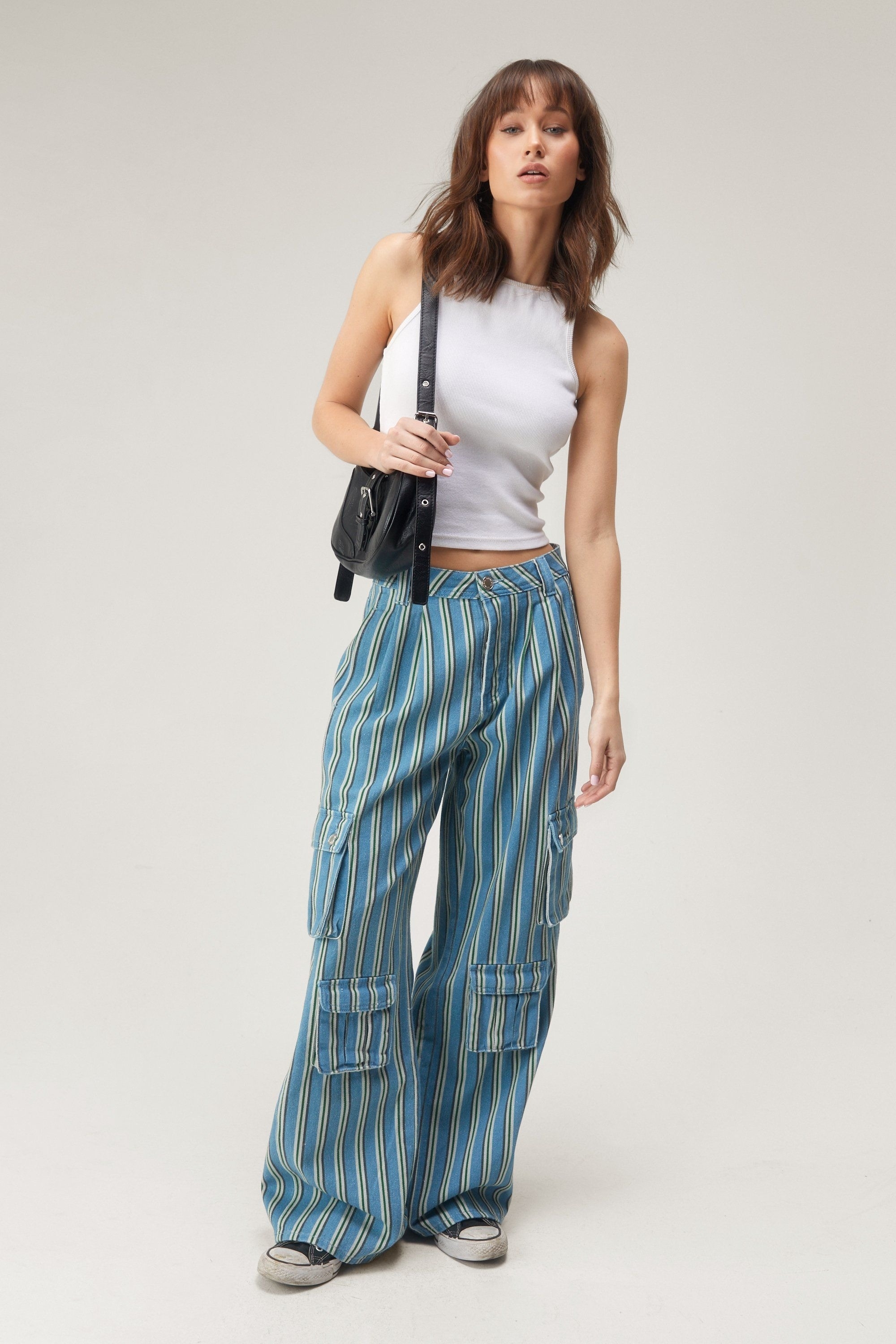 Woman in a white sleeveless top and striped trousers with a shoulder bag, posing for a fashion look