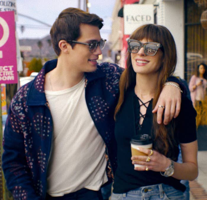 Nicholas Galitzine, Anne Hathaway walking arm in arm, smiling, with bystanders in the background in The Idea of You
