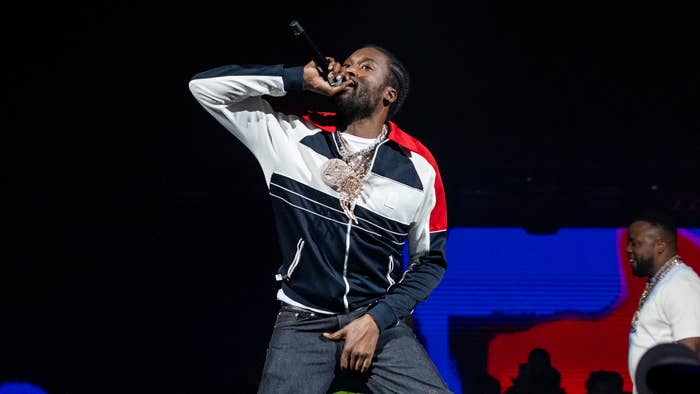 Person on stage singing into a microphone, wearing a track jacket and chain necklace