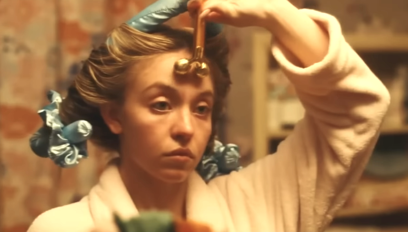 Woman using a jade roller on her face, hair in curlers, focused expression