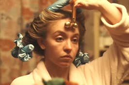 Woman using a jade roller on her face, hair in curlers, focused expression