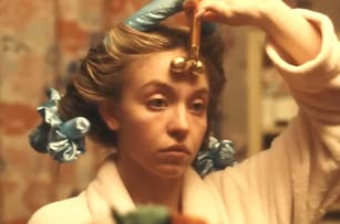 Woman using a jade roller on her face, hair in curlers, focused expression